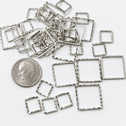 A pile of small silver square metal frames with textured, hammered edges, displayed on a white background next to a US dime for scale. The text 'The Mystical Garden Path' is visible at the bottom.