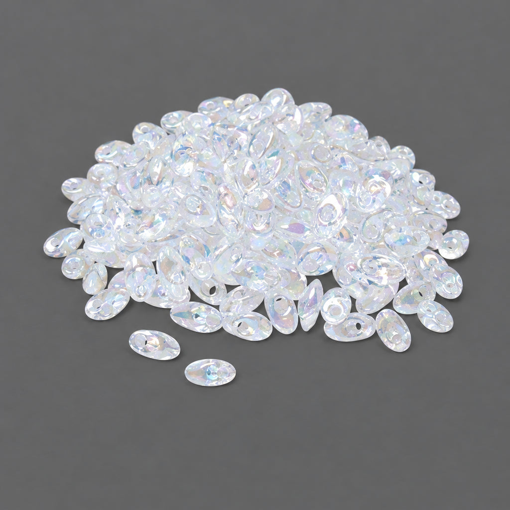 Clear iridescent oval glass beads scattered on a dark gray background, with more beads piled in the upper area.