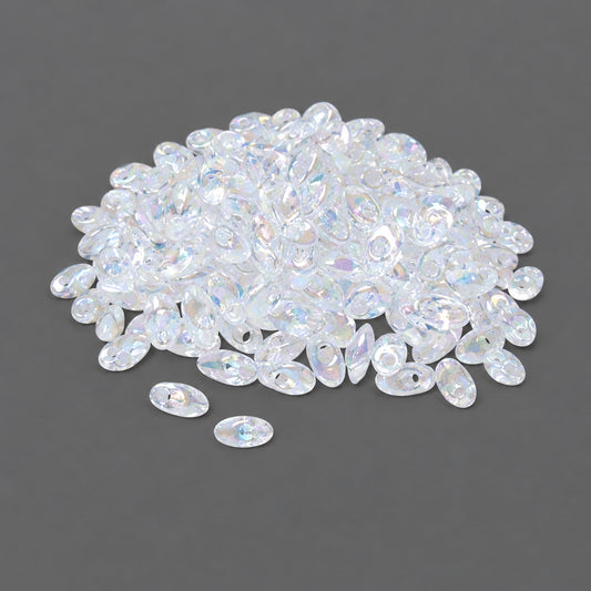Clear iridescent oval glass beads scattered on a dark gray background, with more beads piled in the upper area.