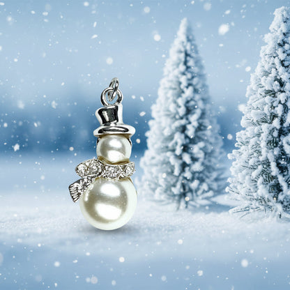 A snowman-shaped pendant charm featuring two cream-colored faux pearls, a silver top hat, and a silver and crystal bow, shown on a light gray textured background.