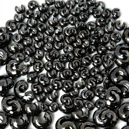A close-up pile of glossy black bead COVERS on a white background.