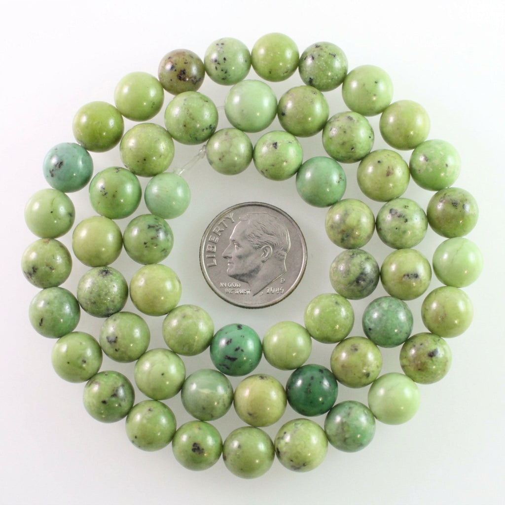 Green stone beads with natural dark inclusions, arranged in a loop around a silver coin for scale on a white background.