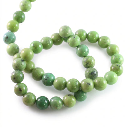 A strand of polished round beads in light to medium green with natural marbling and dark inclusions, arranged on a plain white background.