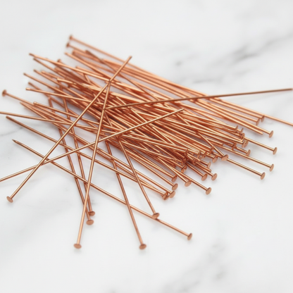 A pile of long, thin copper-colored metal pins with round flat ends, arranged on a white marble surface.