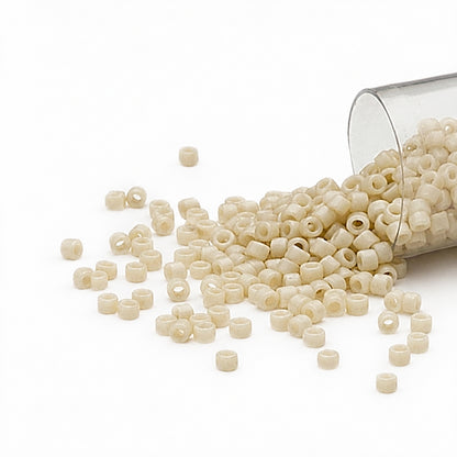 Off-white GLASS seed beads spilling out of a clear plastic cup on a white background.