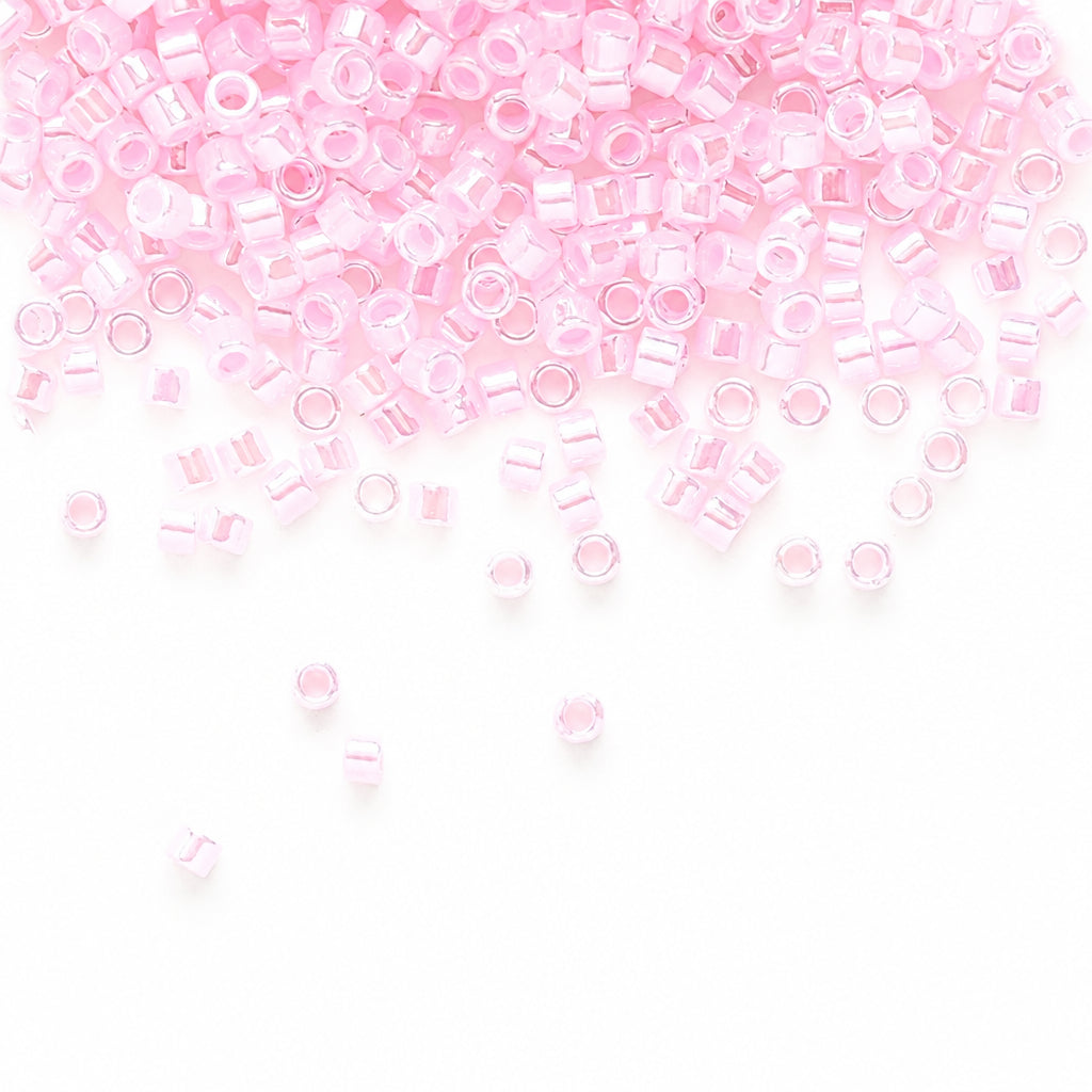 Light pink seed beads scattered across a white background, with more beads concentrated toward the top and a few loose beads near the bottom.