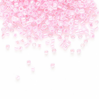Light pink seed beads scattered across a white background, with more beads concentrated toward the top and a few loose beads near the bottom.