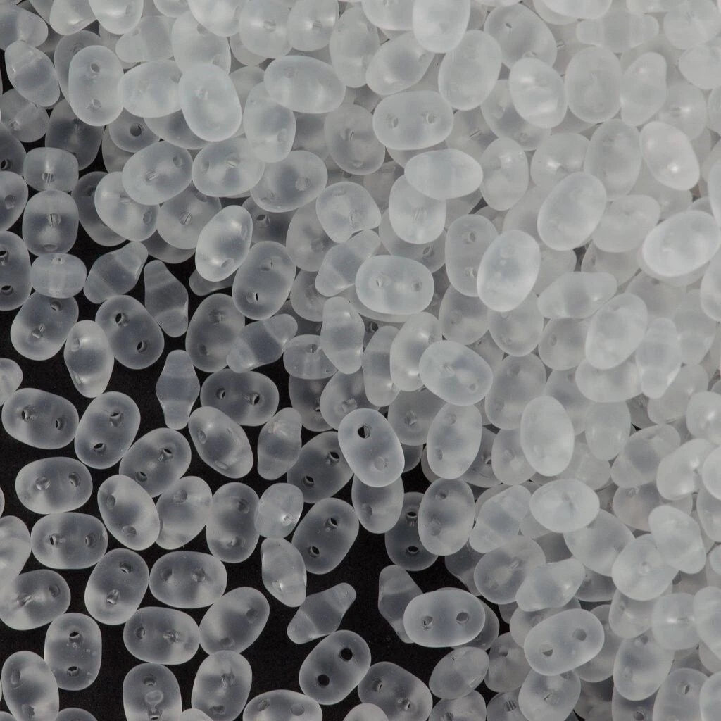 A close-up pile of small, translucent white plastic beads with two holes, shown against a dark background.