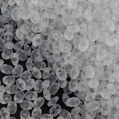 A close-up pile of small, translucent white plastic beads with two holes, shown against a dark background.