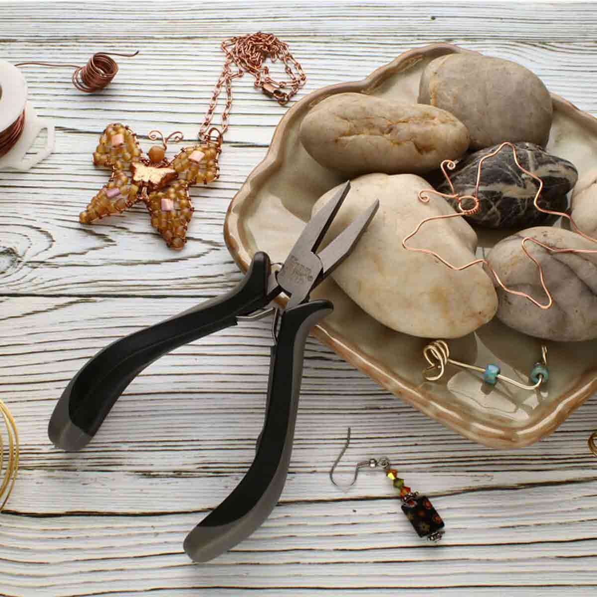 Jewelry-making tools and materials on a wooden surface with pliers, stones, and jewelry components.