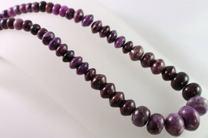 A strand of polished purple and dark maroon beads, likely hematite or a similar stone, arranged in two loops on a white background.