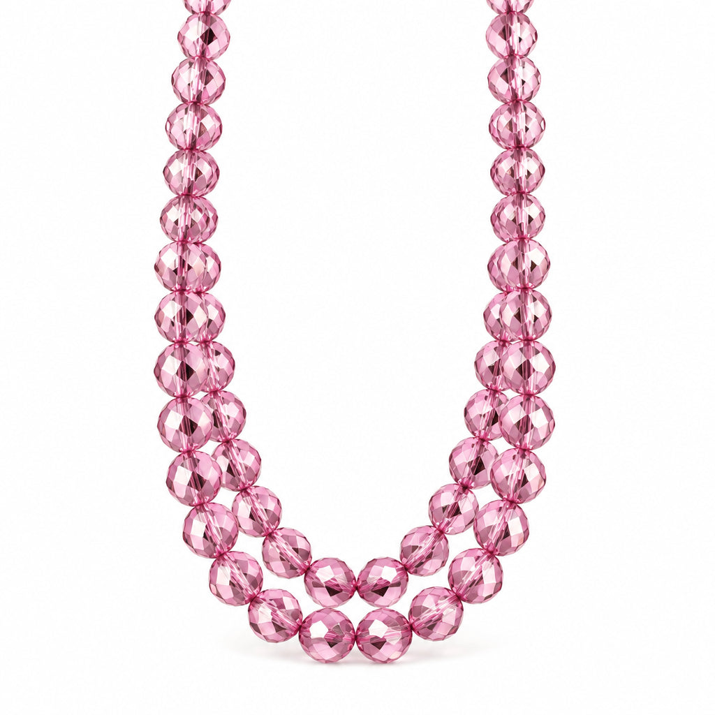 A strand of faceted pink glass beads draped over a white surface with clear acrylic display blocks in the background.