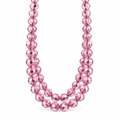 A strand of faceted pink glass beads draped over a white surface with clear acrylic display blocks in the background.