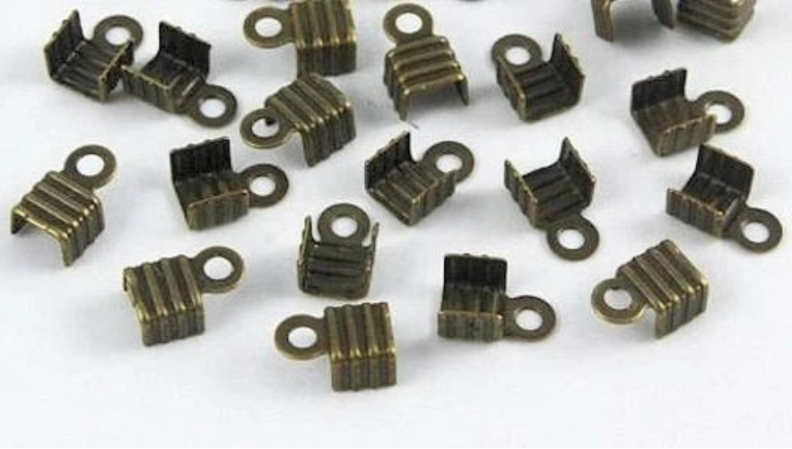 A group of small metallic jewelry findings, specifically U-shaped claw settings with looped prongs, in an antique bronze finish, scattered on a plain white background.