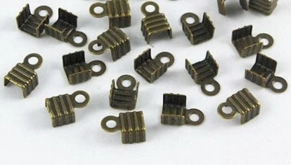 A group of small metallic jewelry findings, specifically U-shaped claw settings with looped prongs, in an antique bronze finish, scattered on a plain white background.