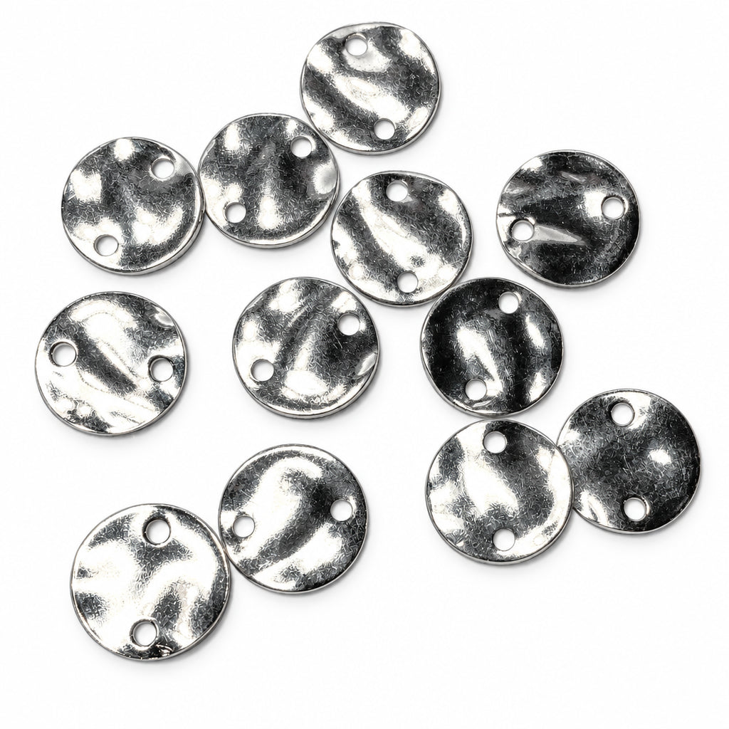 Ten small round silver metal discs with two pre-drilled holes, arranged on a plain light gray background.