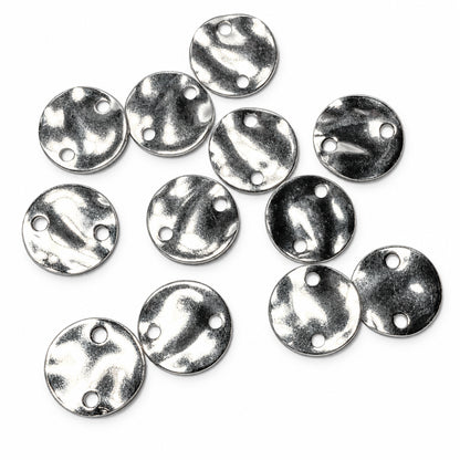 Ten small round silver metal discs with two pre-drilled holes, arranged on a plain light gray background.