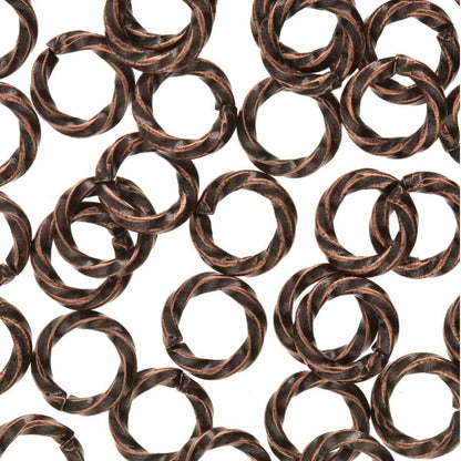A close-up, top-down view of multiple twisted metal jump rings with a dark bronze and copper finish, arranged in a repeating pattern on a solid white background.