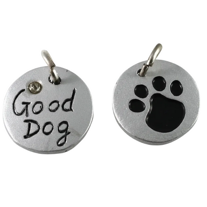 Two round silver metal dog name tags or charms on a white background, one engraved with 'Good Dog' and the other with a black paw print. A coin is partially visible at the bottom for scale.