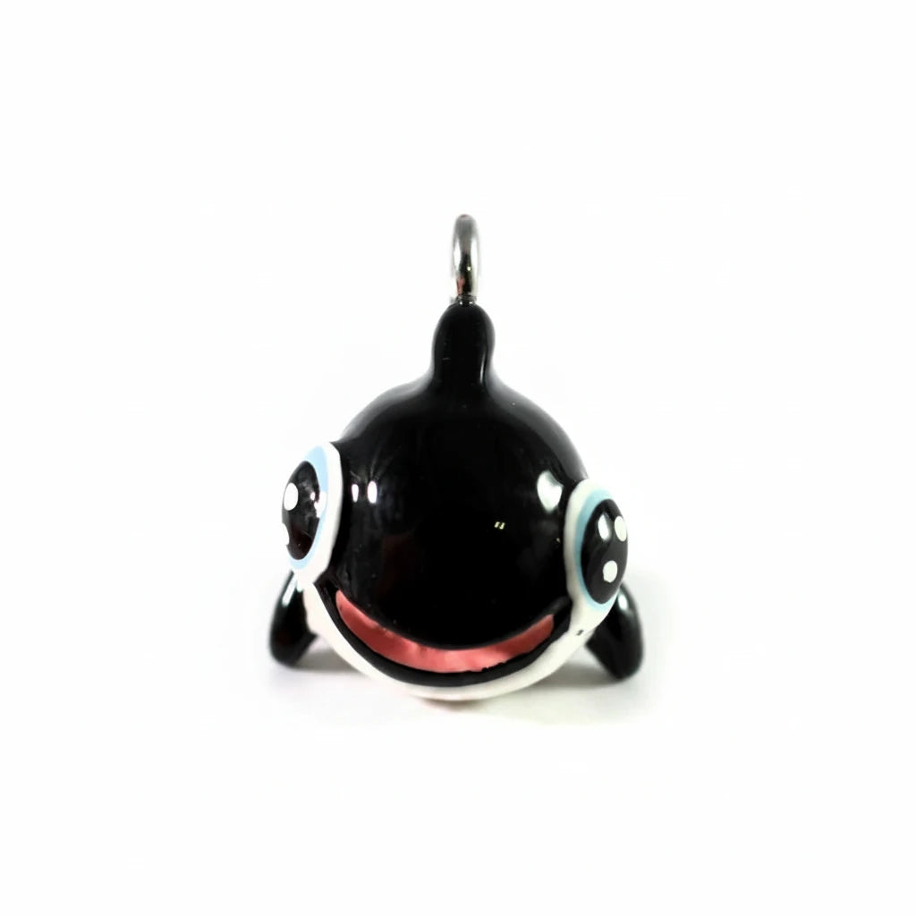 A glossy black charm pendant with large cartoon eyes, a pink tongue, and a silver metal jump ring at the top, shown against a plain white background.