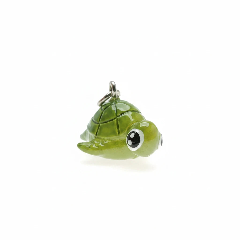 A small glossy green turtle charm with large cartoon eyes and a silver metal loop at the top, photographed on a plain white background.