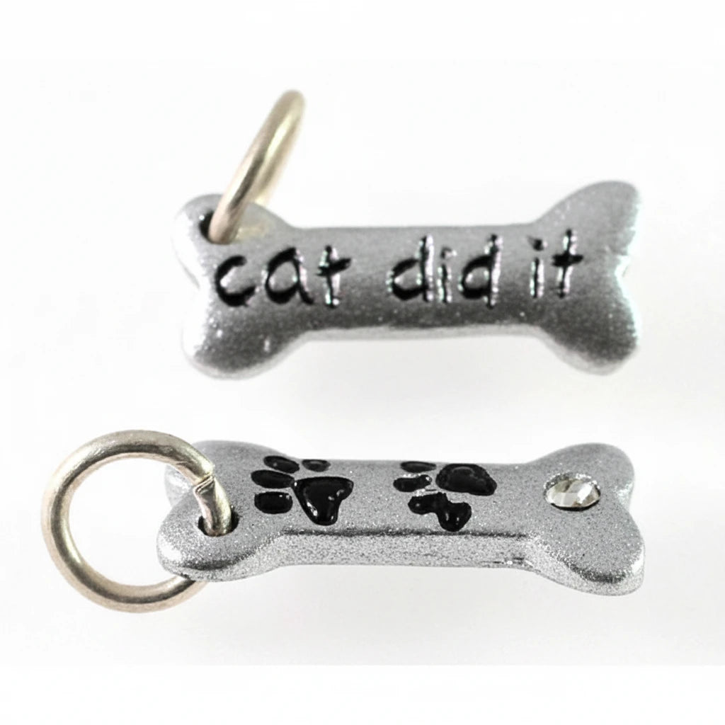 Two silver-tone metal bone-shaped charms on a plain white background. The top charm is engraved with the words 'cat did it' and has a small hanging loop at the top.