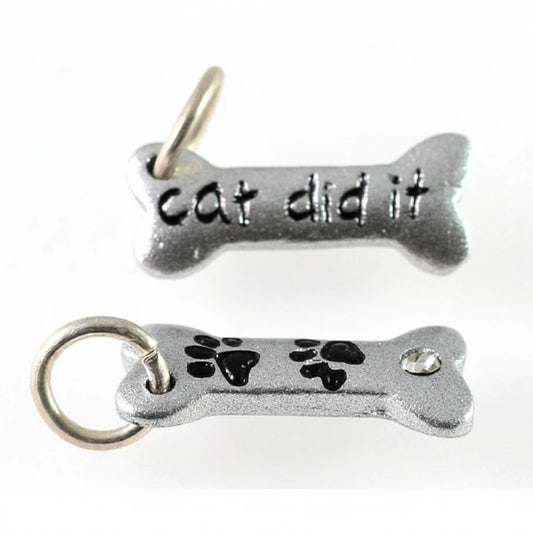 Two silver-tone metal bone-shaped charms on a plain white background. The top charm is engraved with the words 'cat did it' and has a small hanging loop at the top.