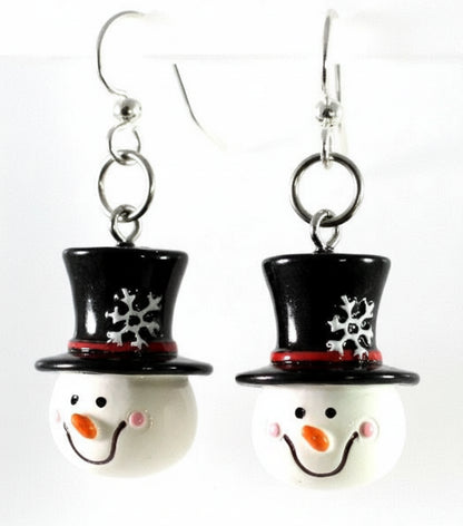 A pair of snowman-themed dangle earrings with black top hats, red bands, and smiling white faces on silver fishhook wires, shown against a plain white background.