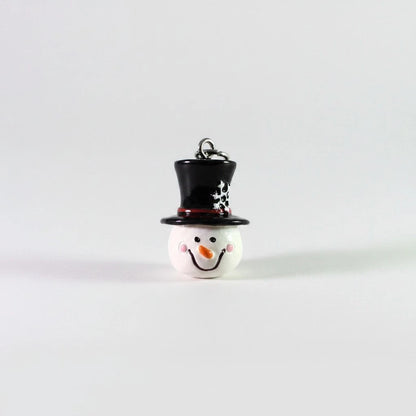 A small snowman ornament or charm with a white round body, black top hat decorated with white polka dots, and a black scarf, shown on a plain light gray background.