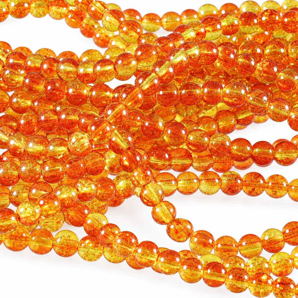 Close-up of strands of round translucent amber-orange beads on a light reflective surface.
