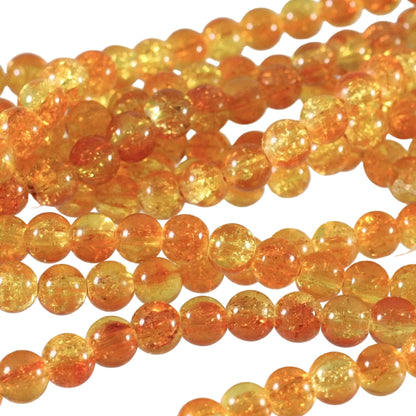 Close-up of strands of round amber-orange glass beads with visible internal glitter and translucent yellow-orange tones on a light background.