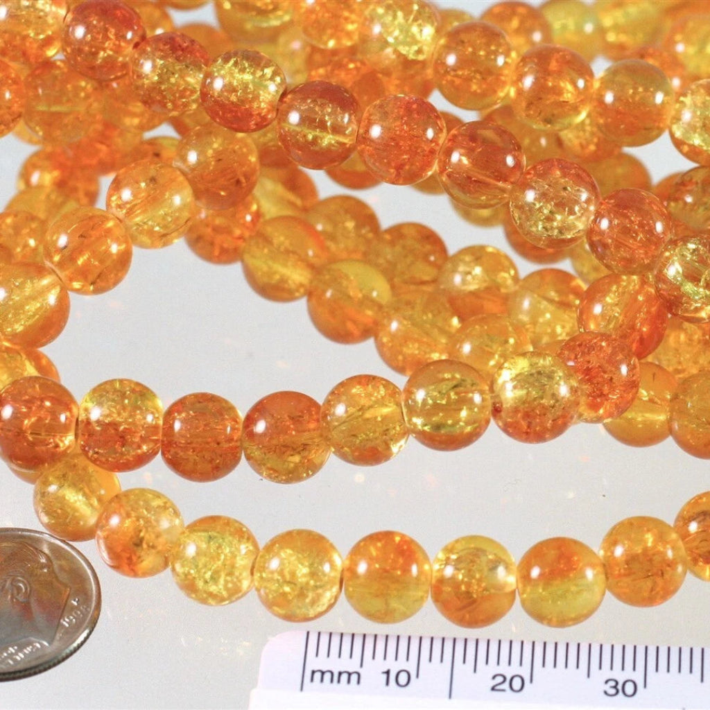 Multiple strands of round, translucent amber-orange beads with tiny inclusions, shown on a white surface with a coin and ruler for scale.