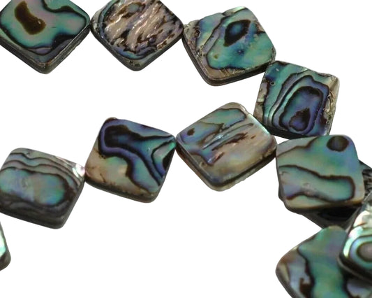Square abalone shell beads with iridescent green, blue, and brown patterns, arranged in a loose curve on a white background.