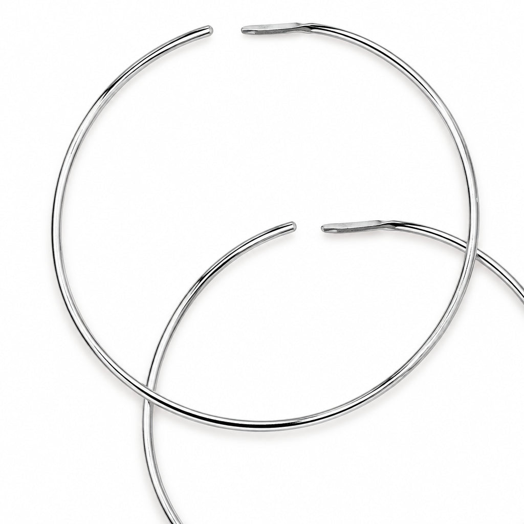 Two thin silver metal hoop earrings overlapping on a plain white background.