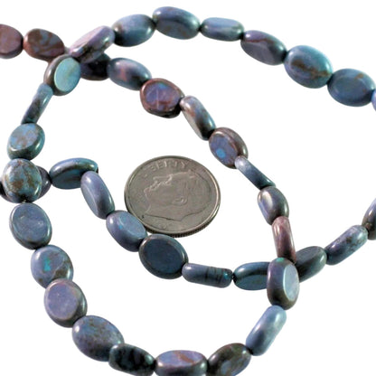 A strand of polished oval beads in a dark iridescent blue-gray color with purple and green flashes, shown next to a US quarter for scale on a white background.