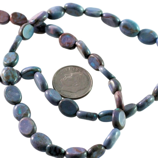 A strand of polished oval beads in a dark iridescent blue-gray color with purple and green flashes, shown next to a US quarter for scale on a white background.