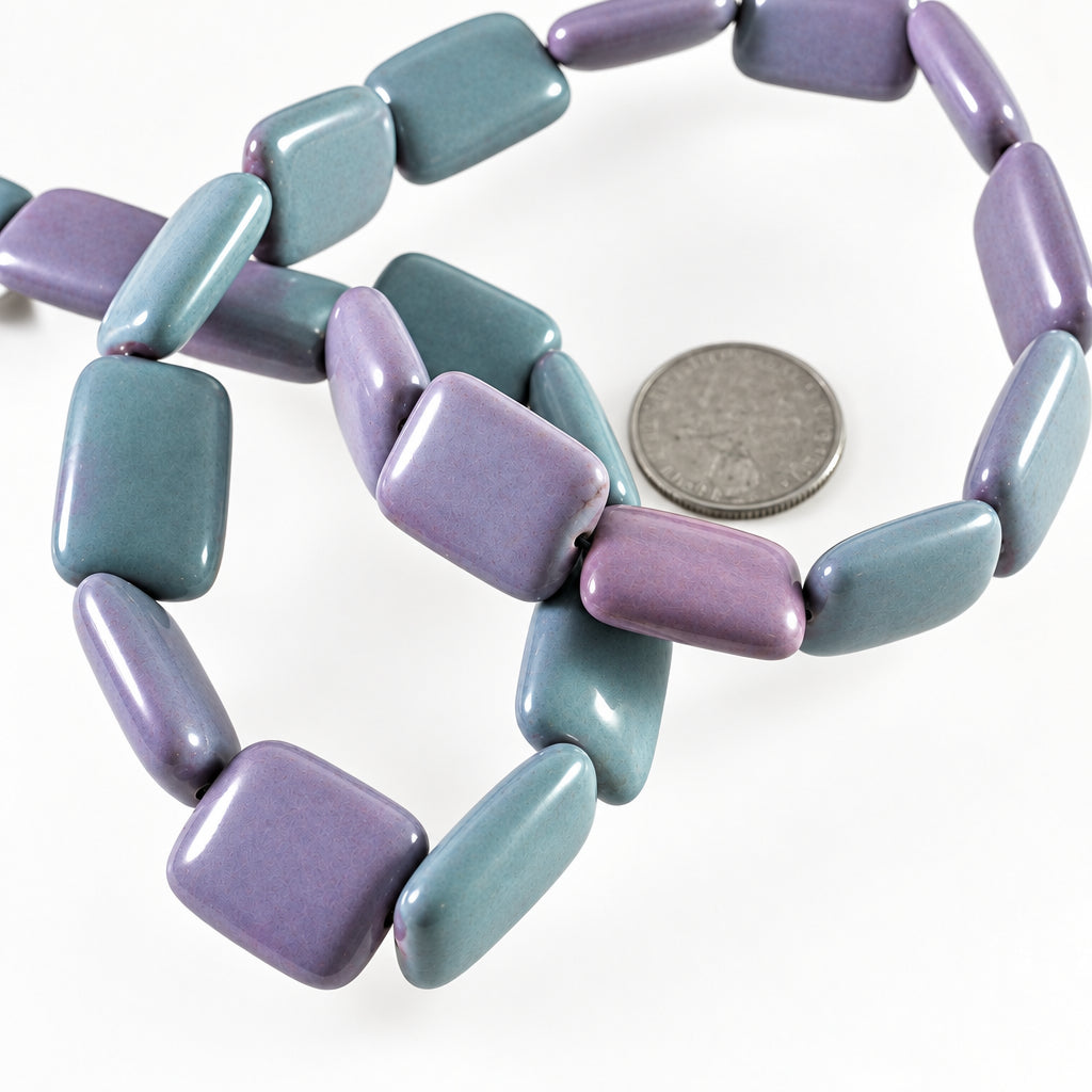 A strand of lavender and purple rectangular cabochon beads with a glossy finish, shown next to a silver coin for scale on a white background.