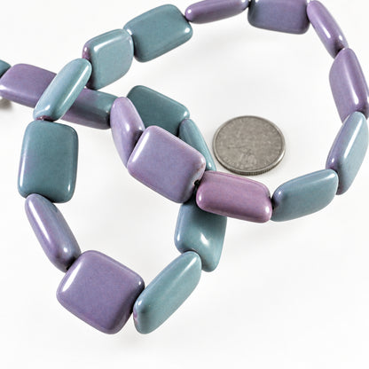 A strand of lavender and purple rectangular cabochon beads with a glossy finish, shown next to a silver coin for scale on a white background.