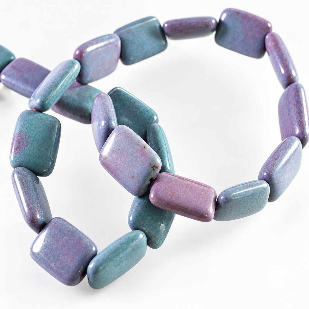 A close-up of a beads made of smooth, polished rectangular beads in shades of lavender purple, dusty blue, and gray, arranged on a plain white background.