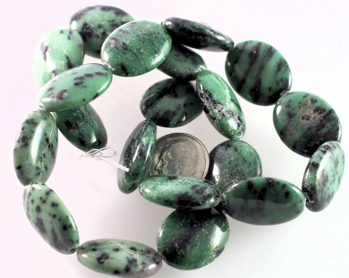 A strand of polished green stone beads with dark natural veining, shown on a plain white background with a coin for scale.