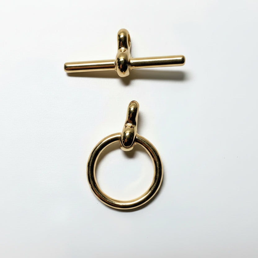 Two polished gold-tone metal jewelry findings on a white background: a toggle clasp at the top and a ring pull at the bottom.