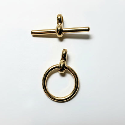 Two polished gold-tone metal jewelry findings on a white background: a toggle clasp at the top and a ring pull at the bottom.