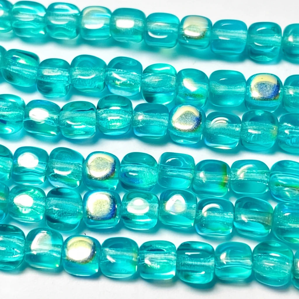 Turquoise blue translucent glass beads with an iridescent finish, arranged in parallel rows on a white background.