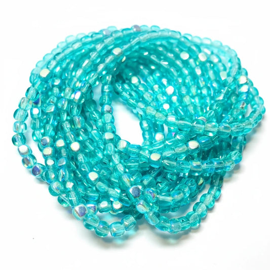 Turquoise blue faceted glass beads with an iridescent finish, arranged in a coil on a white background.