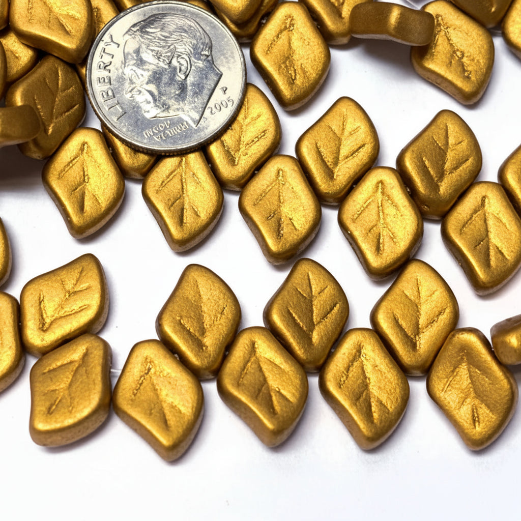 Gold metallic leaf-shaped beads scattered on a white background, with a silver coin placed in the upper left for size reference.