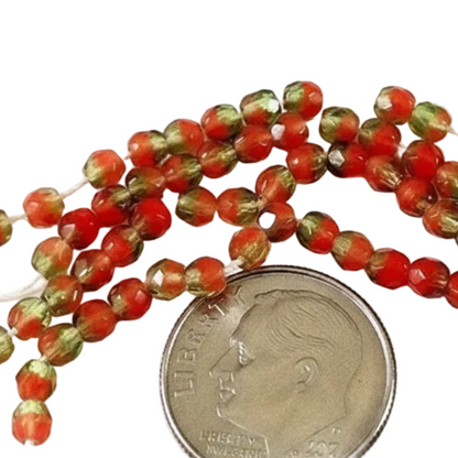 Red and green faceted glass beads on a white background with a US quarter coin for scale.