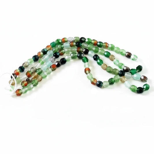 Multicolor faceted gemstone beads in green, black, red, and brown, arranged in strands with a US quarter coin for scale, on a white background with 'The Mystical Garden Path' text overlay.