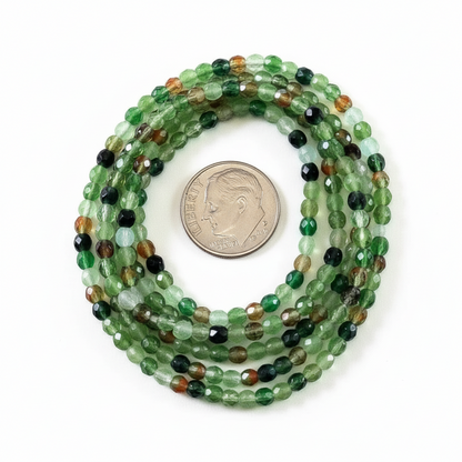 A coiled strand of faceted green gemstone beads with mixed earthy tones, shown next to a US dime for scale on a plain white background.
