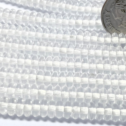 Clear round seed beads strung in multiple rows, with a silver coin in the top right for scale.