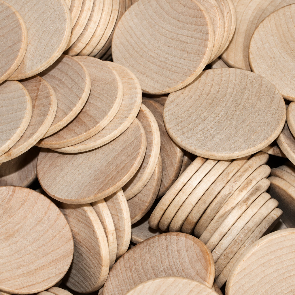 A pile of unfinished light wood round discs, likely plywood or MDF craft blanks, showing natural grain and a pale tan color.